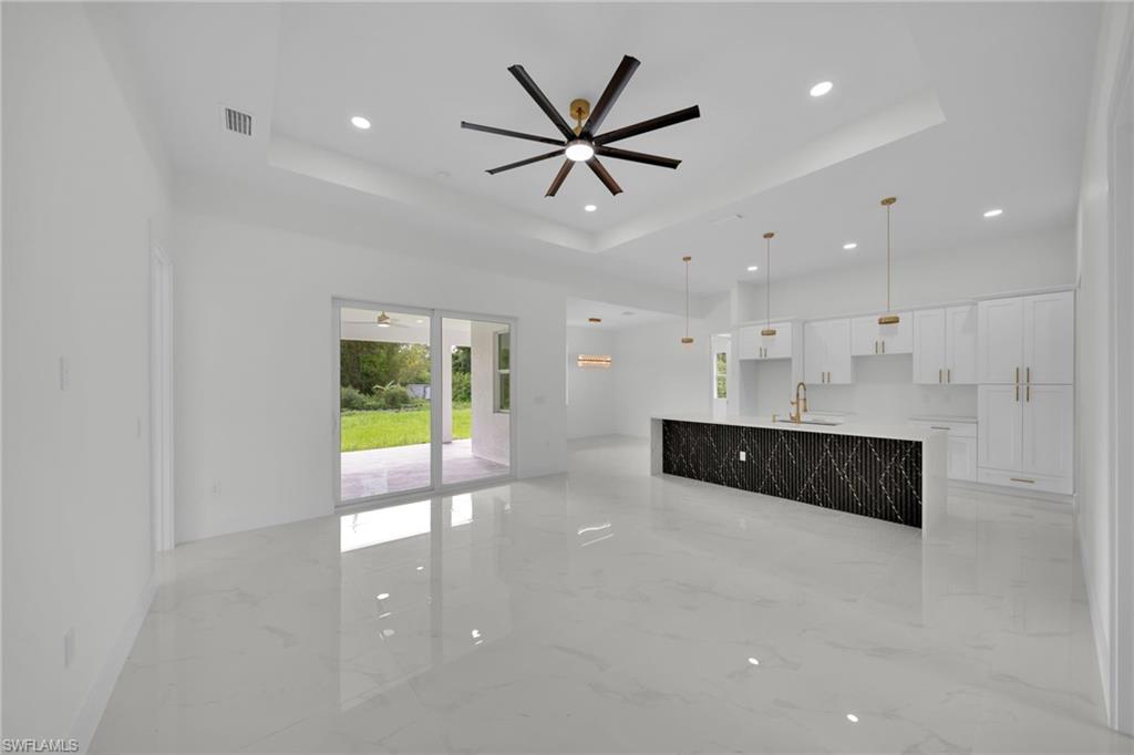 Unfurnished living room featuring light marble finish flooring, a tray ceiling, ceiling fan, and recessed lighting