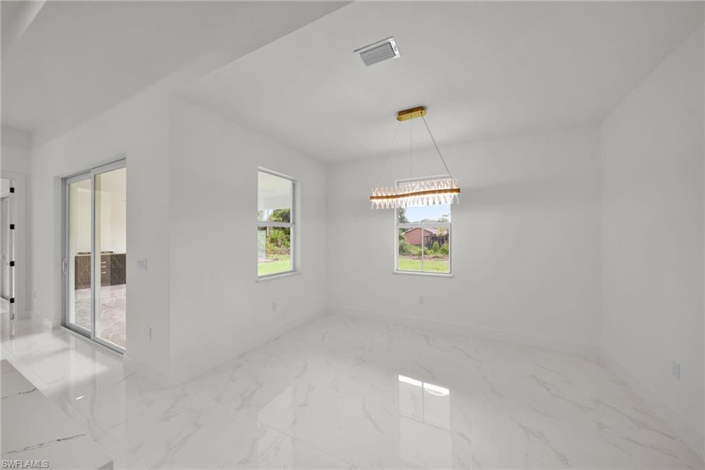 Spare room featuring marble finish floors and a chandelier