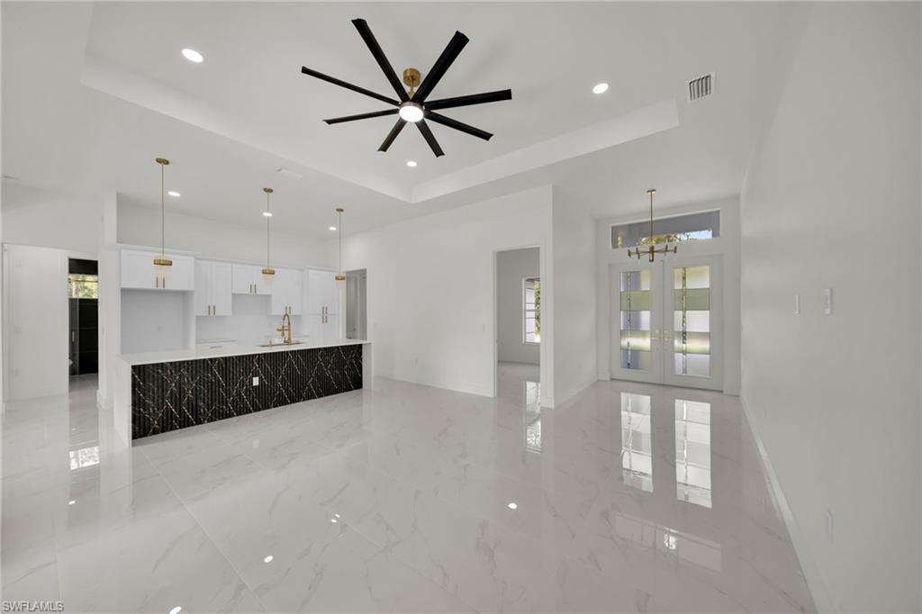 Unfurnished living room featuring a tray ceiling, recessed lighting, french doors, light marble finish flooring, and a chandelier