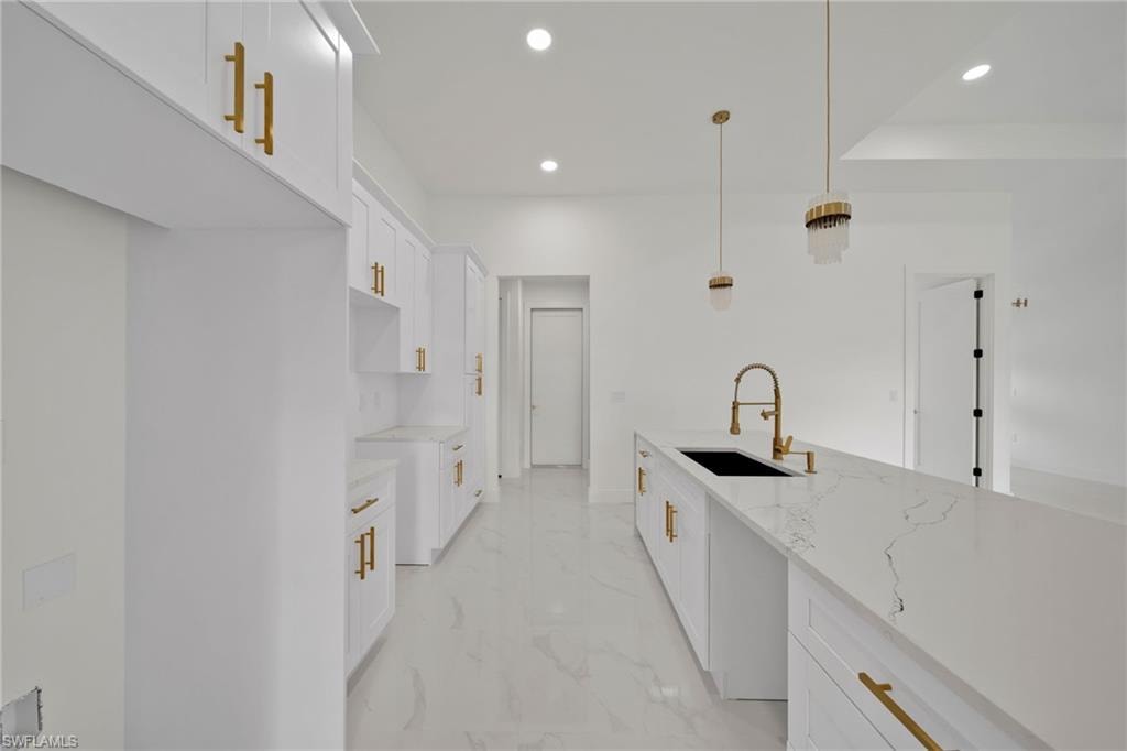Kitchen with light marble finish floors, recessed lighting, light stone countertops, white cabinetry, and decorative light fixtures
