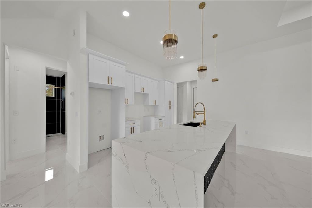 Kitchen with recessed lighting, light marble finish floors, white cabinets, light stone counters, and a center island with sink