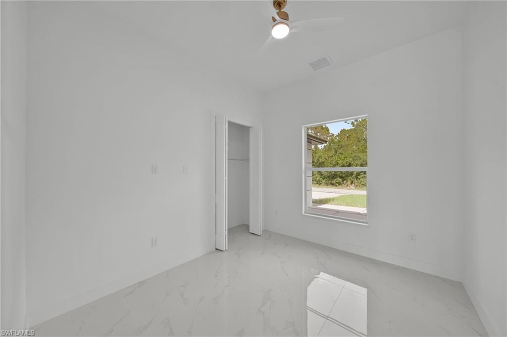 Unfurnished bedroom featuring marble tiled floors, ceiling fan, and a closet