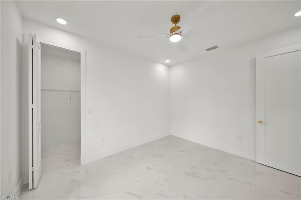 Unfurnished bedroom featuring light marble finish flooring, recessed lighting, a spacious closet, and a ceiling fan