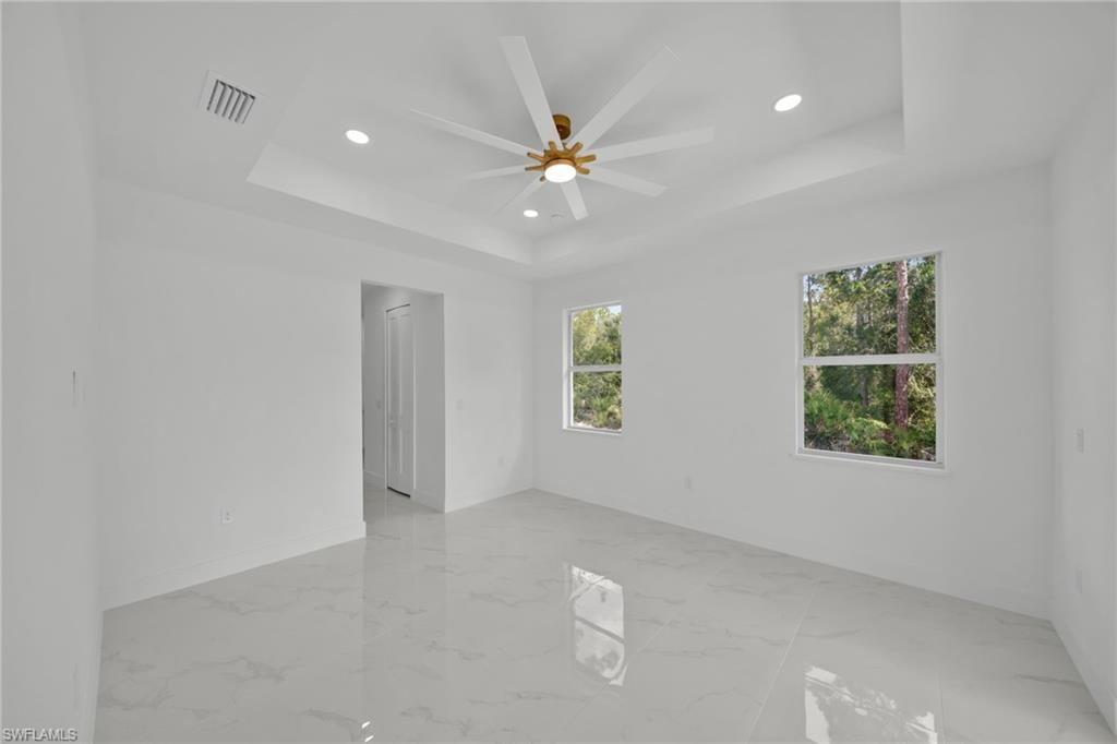 Unfurnished room with a raised ceiling, recessed lighting, ceiling fan, and light marble finish flooring