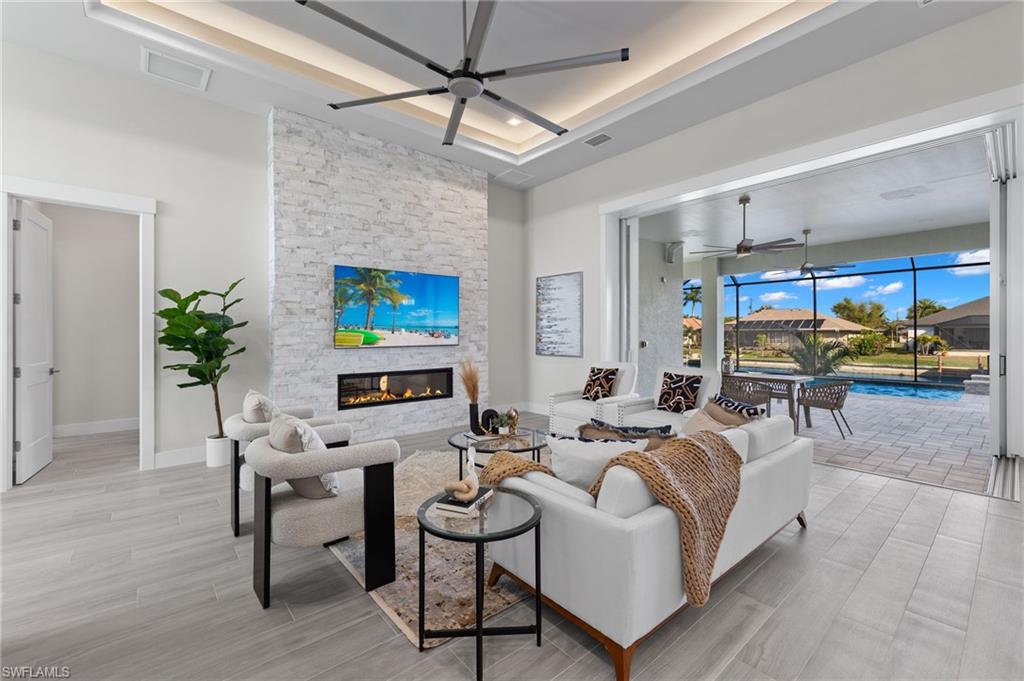 Living room featuring ceiling fan, a fireplace, a tray ceiling
