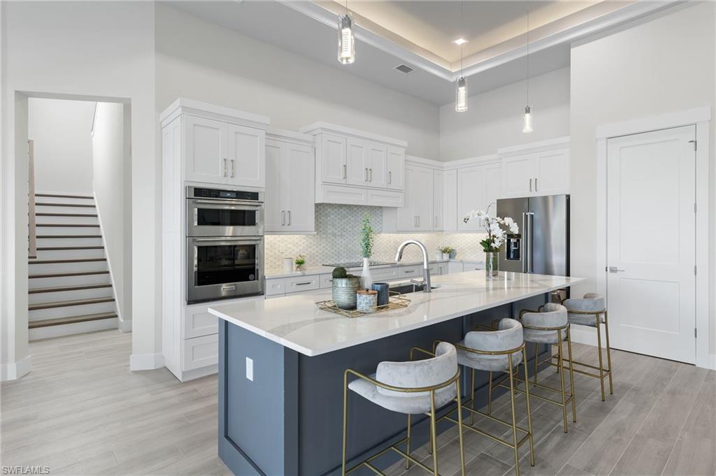 Kitchen featuring appliances with stainless steel finishes, a kitchen breakfast bar, a kitchen island with sink, white cabinets, and hanging light fixtures