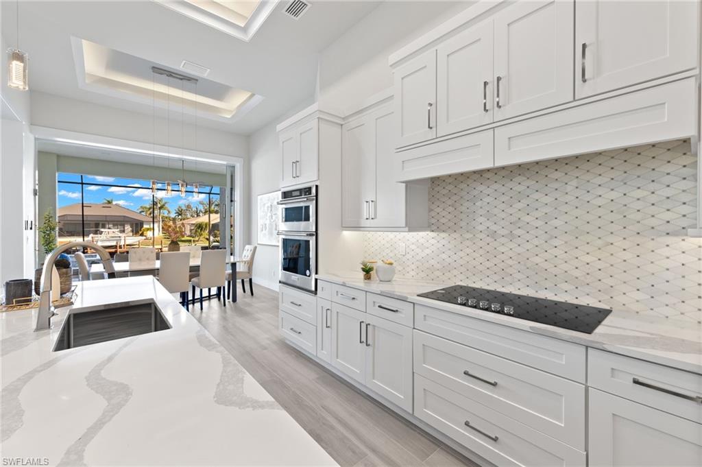 Kitchen featuring backsplash, light stone counters, sink, light hardwood / wood-style flooring, and white cabinetry