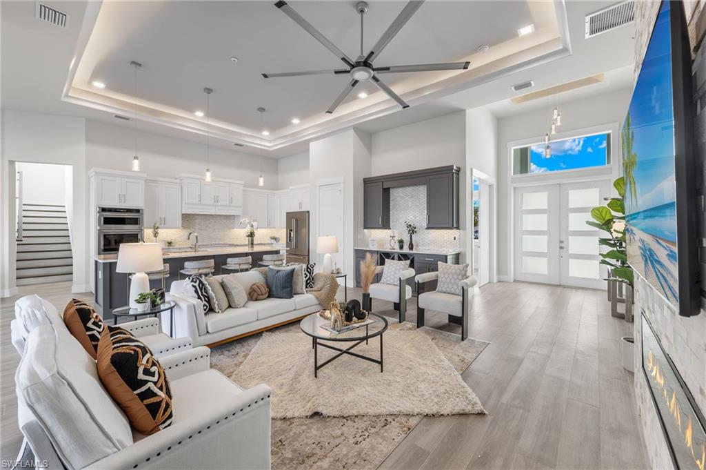 Living room with french doors, a towering ceiling, a raised ceiling, ceiling fan, and plank ceramic tile flooring