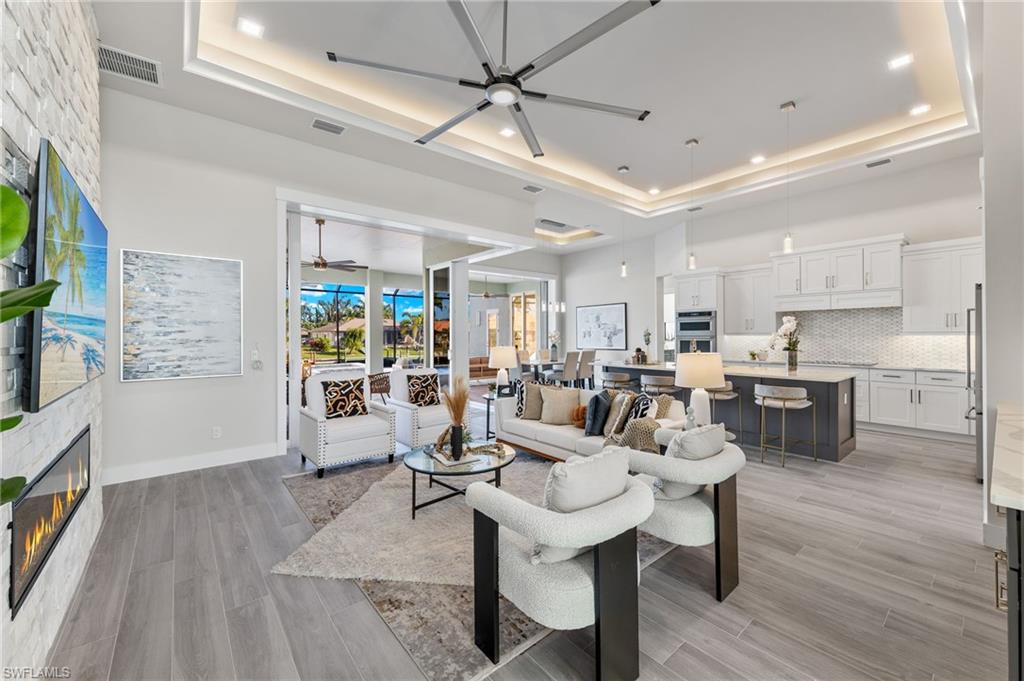 Living room featuring ceiling fan, light plank ceramic tile flooring, a fireplace, and a tray ceiling