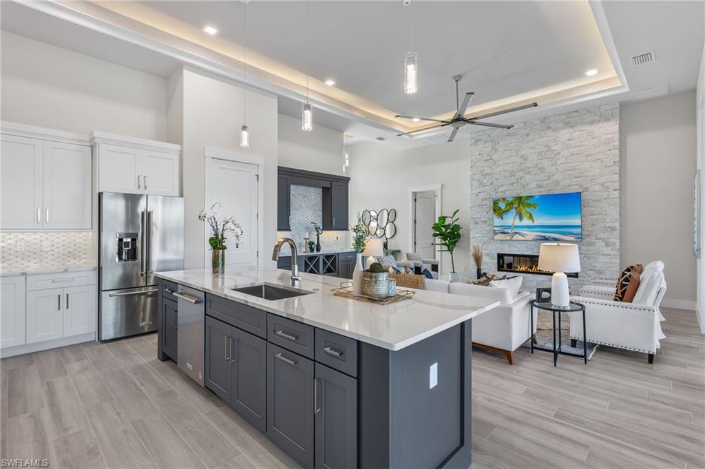 Kitchen with white cabinetry, sink, hanging light fixtures, high end refrigerator, and a center island with sink