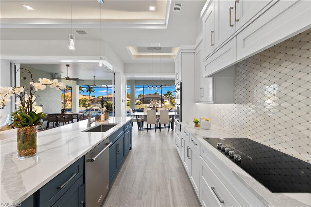 Kitchen with white cabinets, sink, stainless steel dishwasher, decorative backsplash, and light stone counters