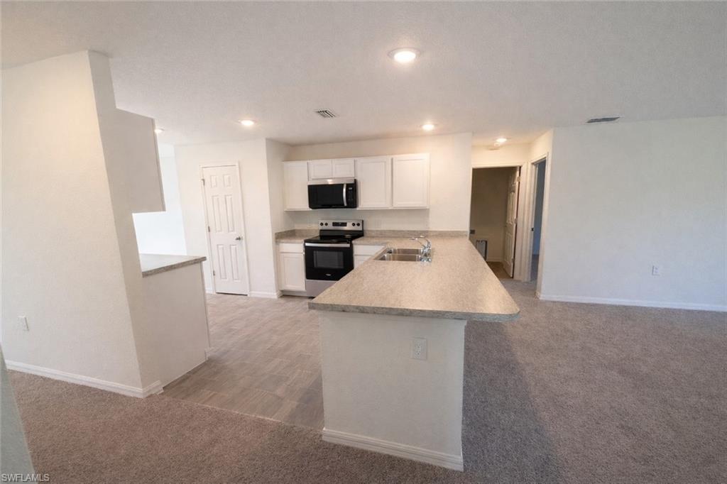 Kitchen with a peninsula, light countertops, white cabinetry, stainless steel appliances, and light carpet