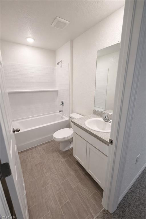 Bathroom with vanity, bathing tub / shower combination, a textured wall, and a textured ceiling