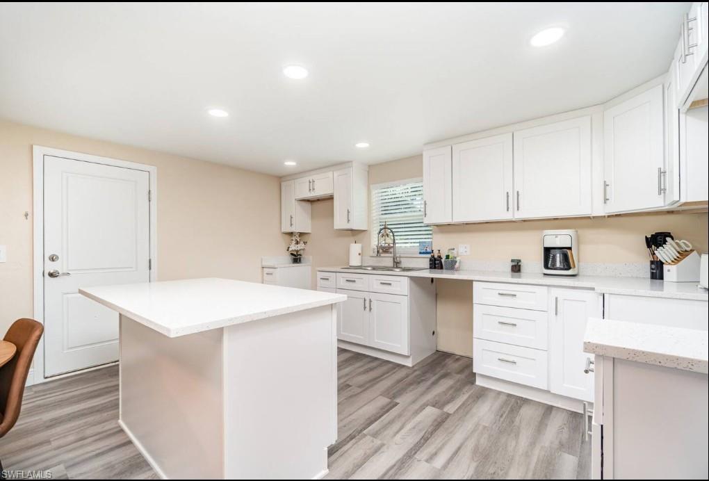 Kitchen with recessed lighting, white cabinetry, a kitchen island, light wood-style flooring, and light stone countertops