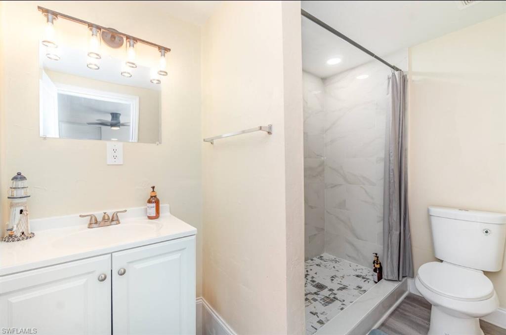 Full bath featuring a tile shower, vanity, and wood finished floors