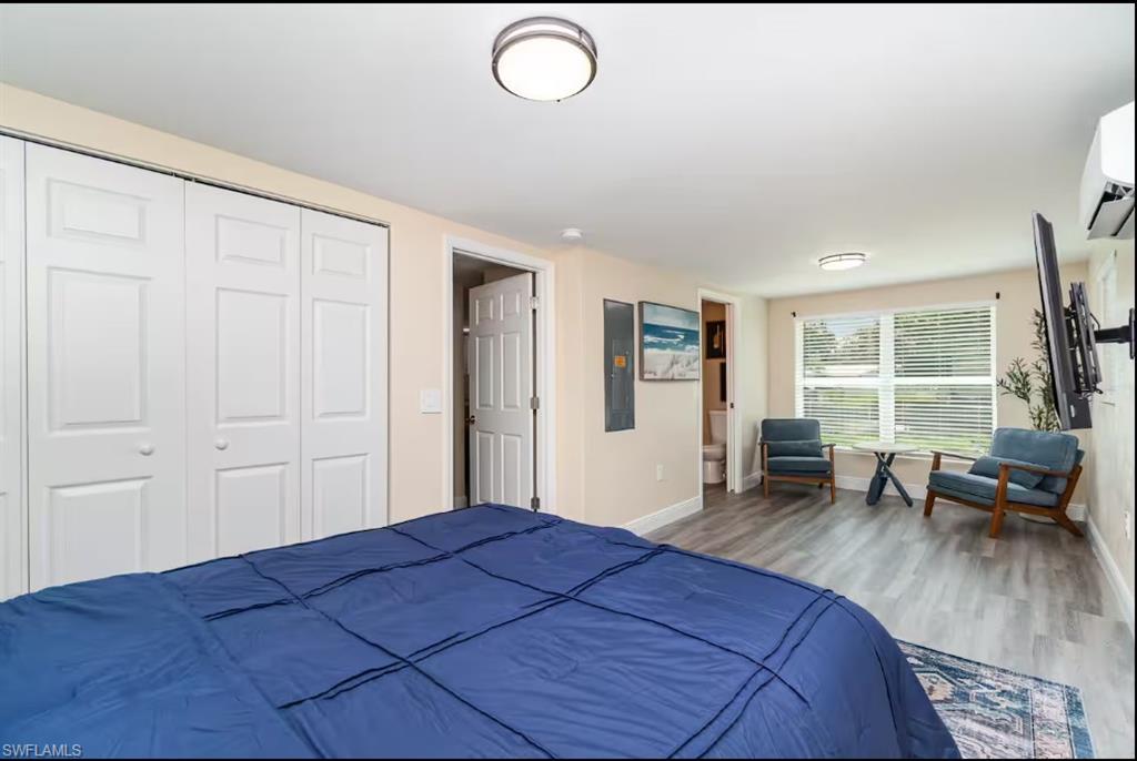 Bedroom featuring wood finished floors, a closet, a wall unit AC, and electric panel