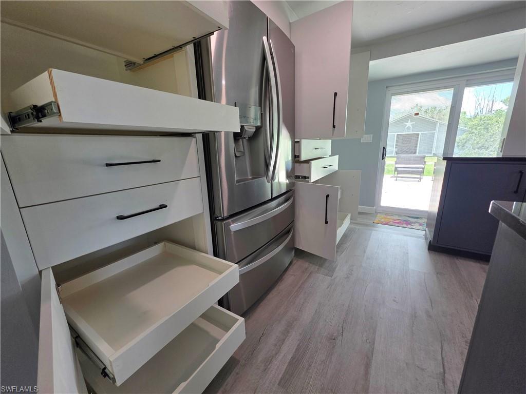 Kitchen with light wood-style flooring, stainless steel fridge with ice dispenser, and white cabinetry