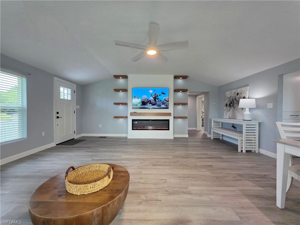 Living room with vaulted ceiling, a ceiling fan, wood finished floors, and a glass covered fireplace