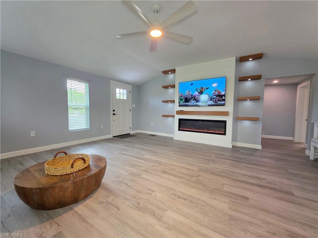 Living area featuring vaulted ceiling, a glass covered fireplace, ceiling fan, and wood finished floors