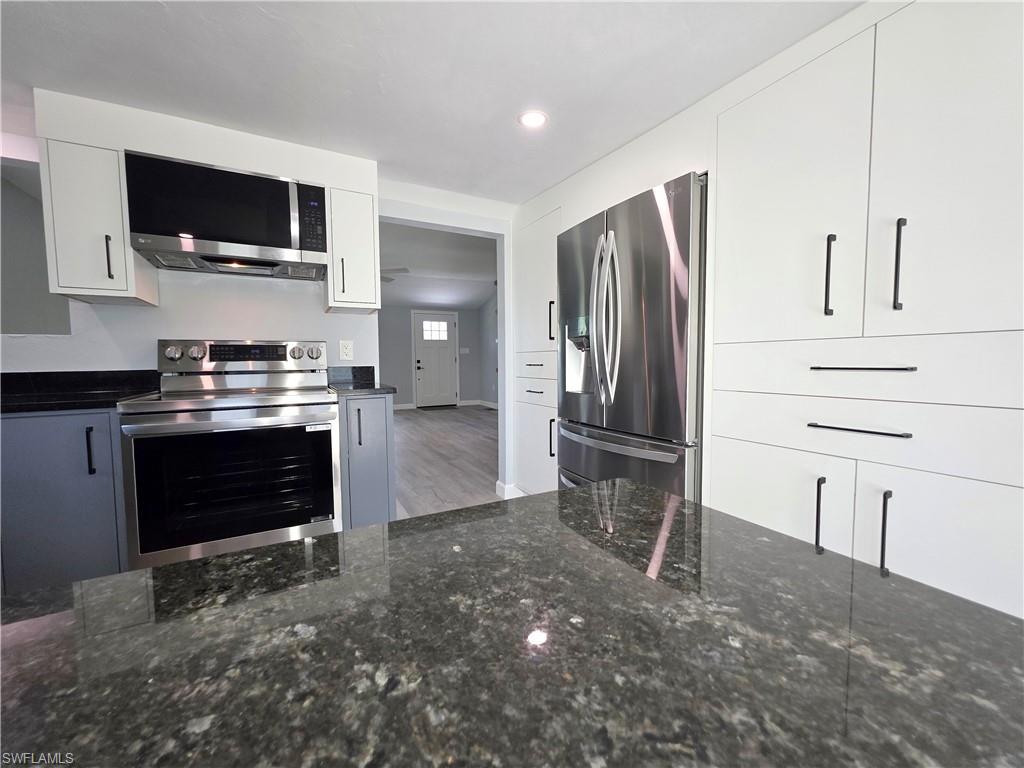 Kitchen with appliances with stainless steel finishes, dark stone counters, white cabinetry, wood finished floors, and recessed lighting