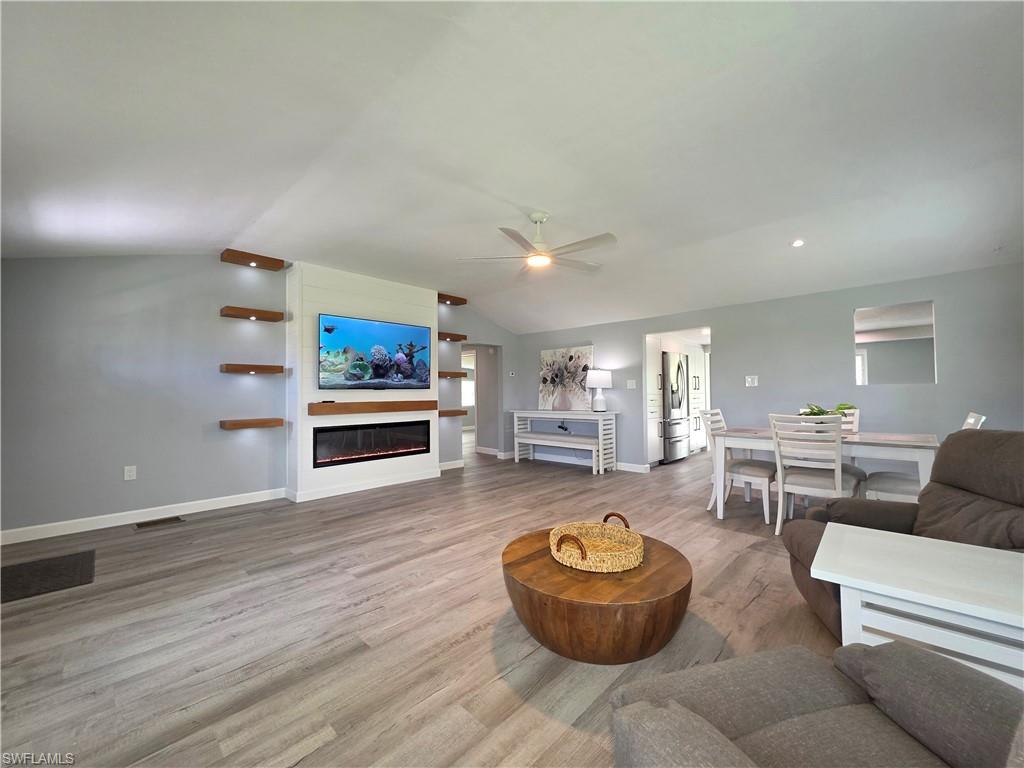 Living area featuring lofted ceiling, wood finished floors, a ceiling fan, a glass covered fireplace, and recessed lighting