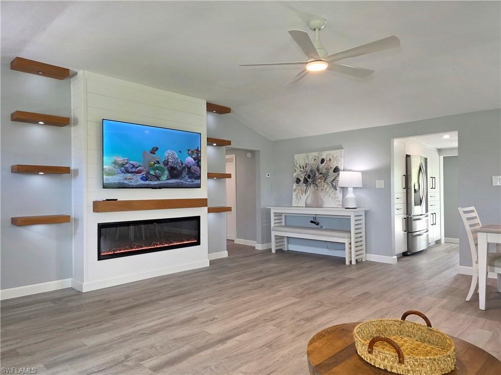 Living room featuring a ceiling fan, wood finished floors, lofted ceiling, and a glass covered fireplace