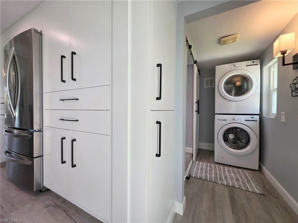 Laundry room with stacked washer / drying machine, wood finished floors, and a barn door