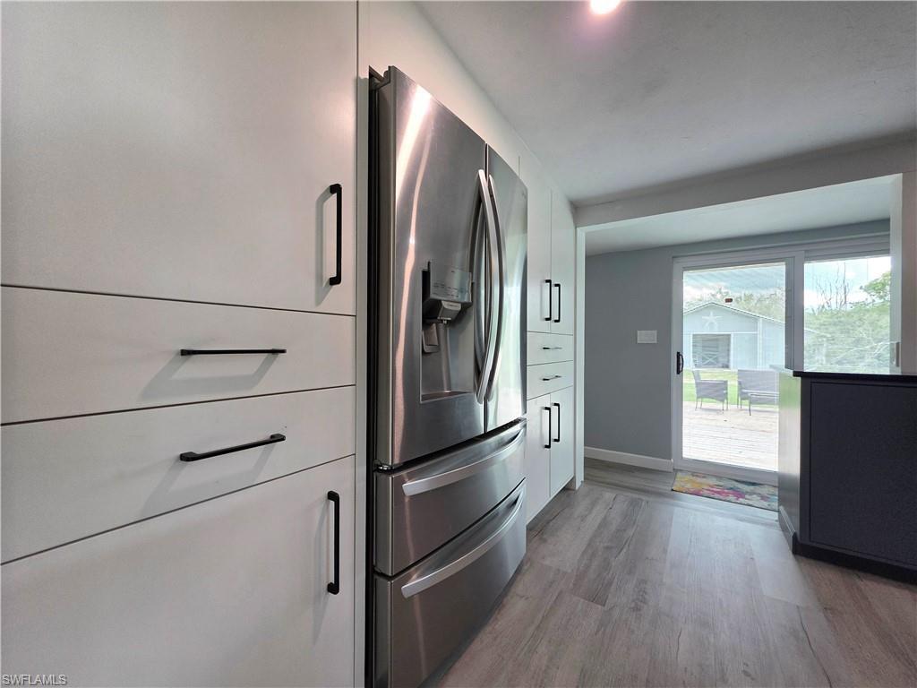 Kitchen view of stainless steel fridge, light wood finished floors, and white cabinets