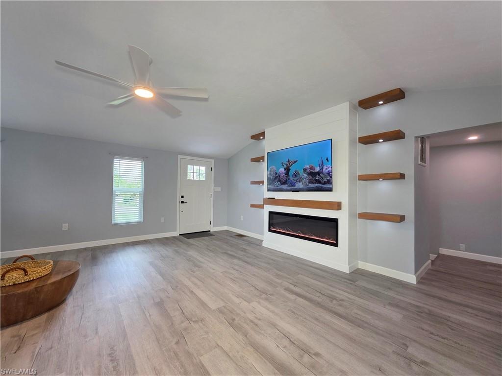 Unfurnished living room featuring lofted ceiling, a ceiling fan, wood finished floors, and a glass covered fireplace