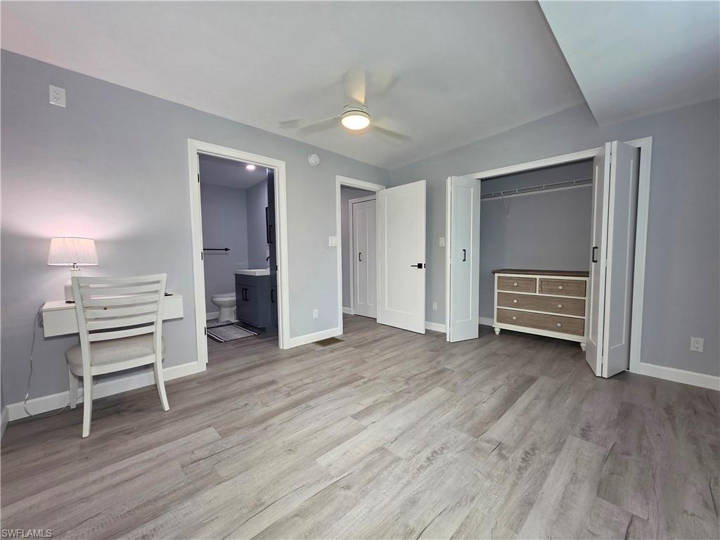 Unfurnished bedroom featuring wood finished floors, a closet, ensuite bath, and a ceiling fan