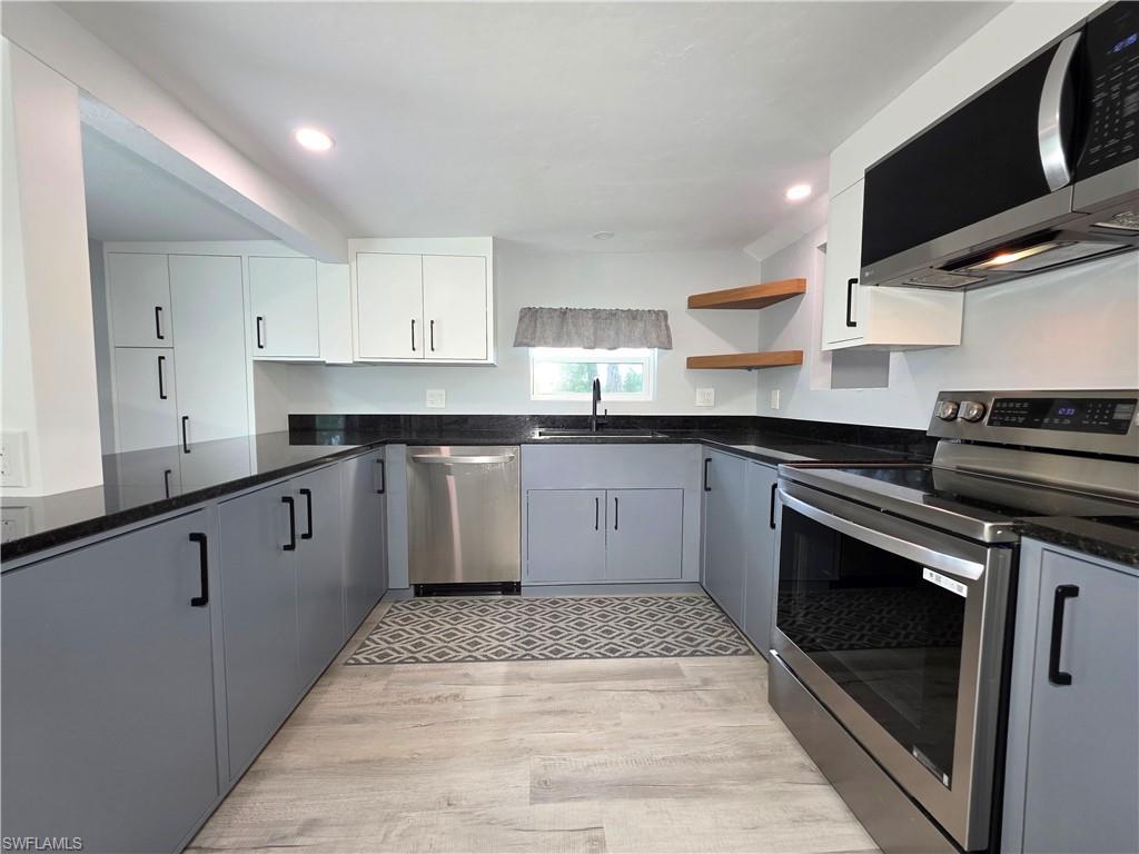Kitchen featuring appliances with stainless steel finishes, light wood-style flooring, open shelves, recessed lighting, and dark stone counters