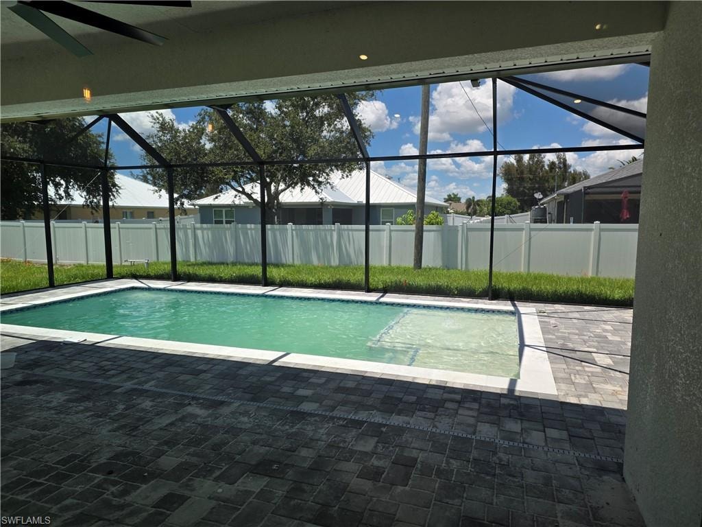Screened swimming pool enclosure featuring a rectangular pool with an integrated sun shelf, paver decking, and a white privacy fence