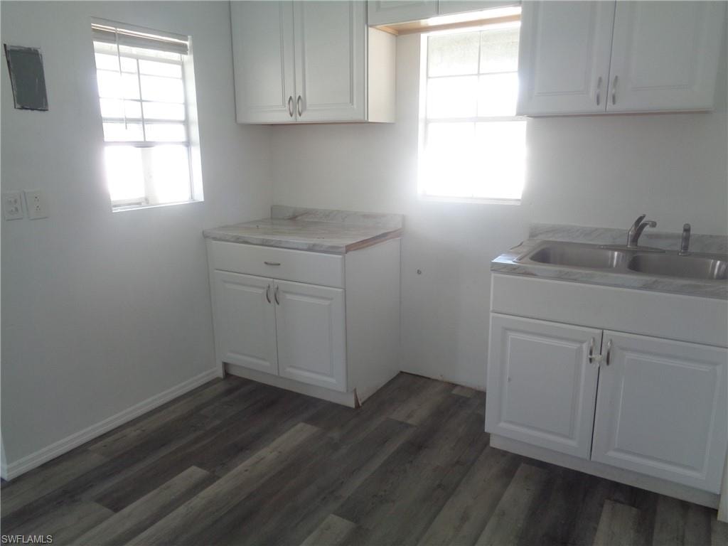 Permitted apartment kitchen featuring light countertops, white cabinetry, dark wood-style floors, and electric panel
