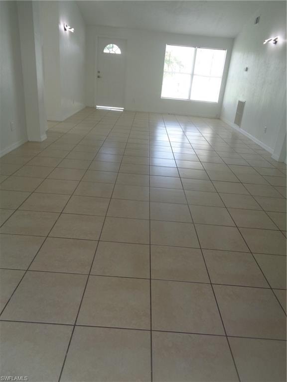 Empty room featuring vaulted ceiling, healthy amount of natural light, and light tile patterned floors