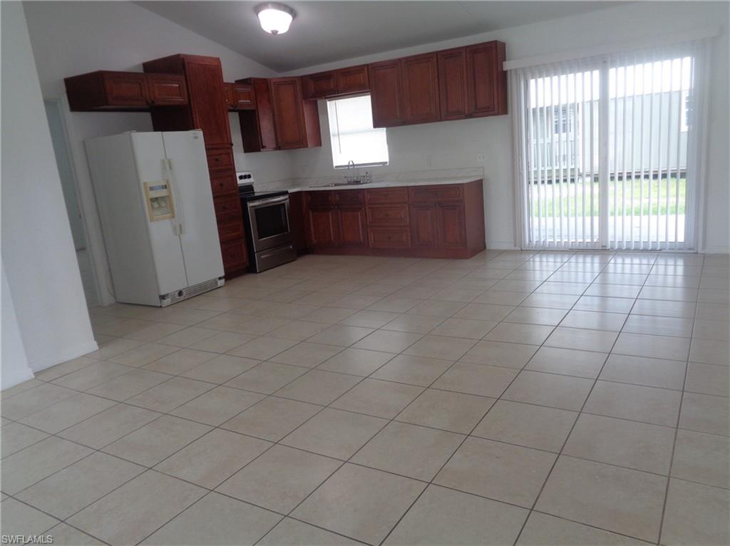 Kitchen featuring white refrigerator with ice dispenser, electric range, lofted ceiling, light tile patterned floors, and light countertops
