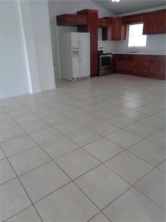 Kitchen with fridge, lofted ceiling, range, light tile patterned floors, and light countertops
