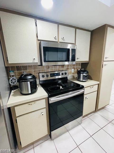 Kitchen featuring appliances with stainless steel finishes, light countertops, light tile patterned floors, and tasteful backsplash