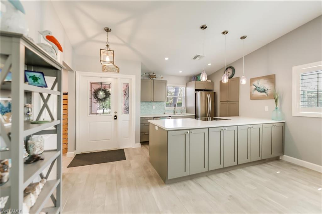 Kitchen featuring lofted ceiling, gray cabinetry, a peninsula, light countertops, and decorative backsplash