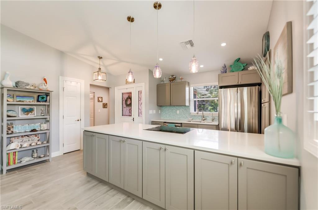 Kitchen with decorative backsplash, freestanding refrigerator, gray cabinets, light countertops, and light wood finished floors