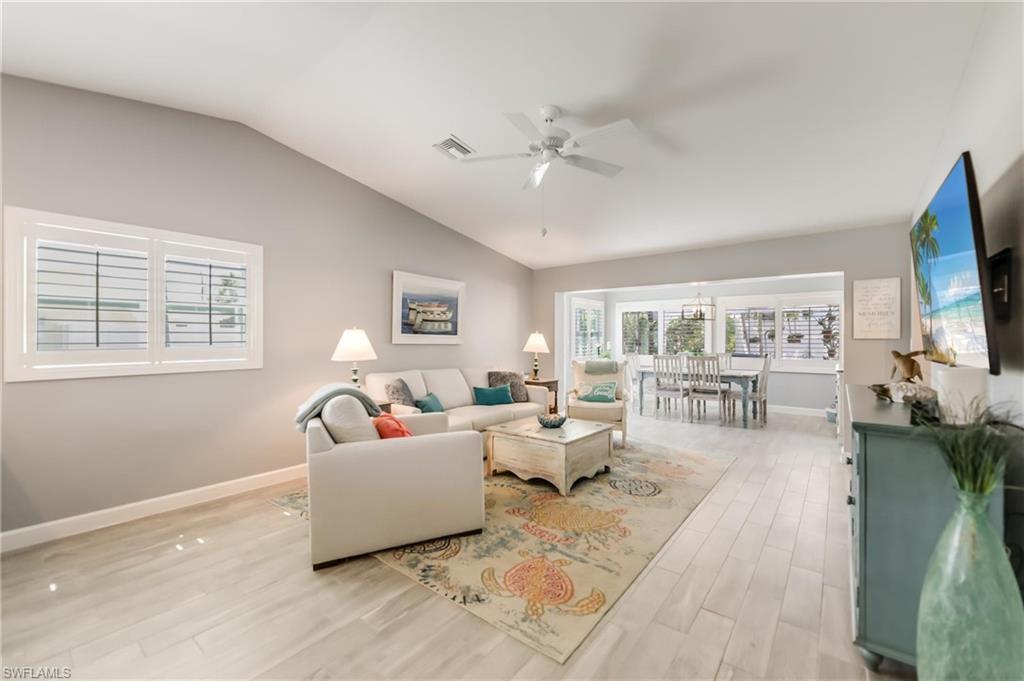 Living room featuring vaulted ceiling, healthy amount of natural light, light wood finished floors, a ceiling fan, and a chandelier