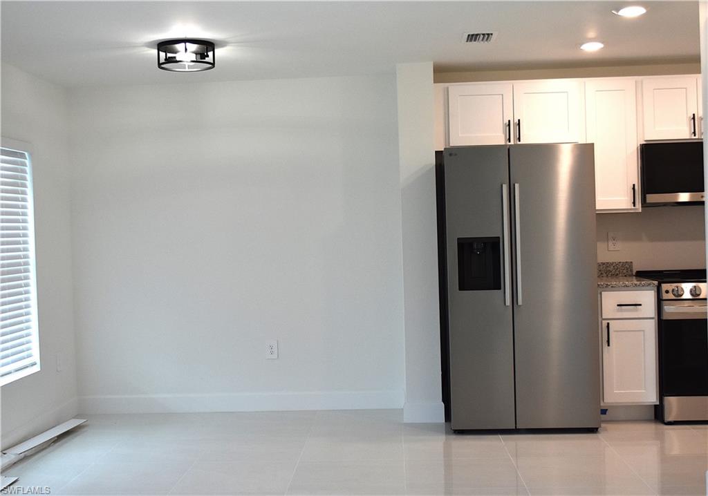 Kitchen with stainless steel appliances, recessed lighting, white cabinets, light tile patterned flooring, and dark stone counters