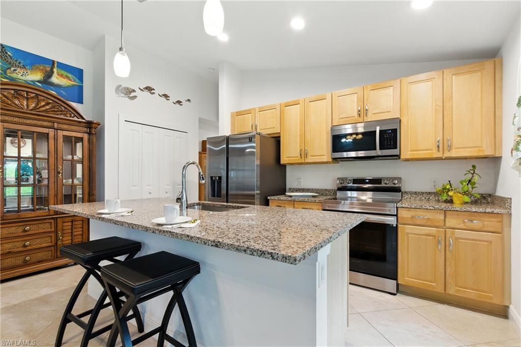 Kitchen with appliances with stainless steel finishes, a kitchen bar, light stone counters, an island with sink, and light tile patterned flooring