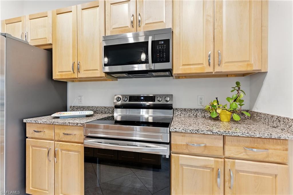 Kitchen featuring stainless steel appliances, light brown cabinetry, light stone countertops, and tile patterned floors