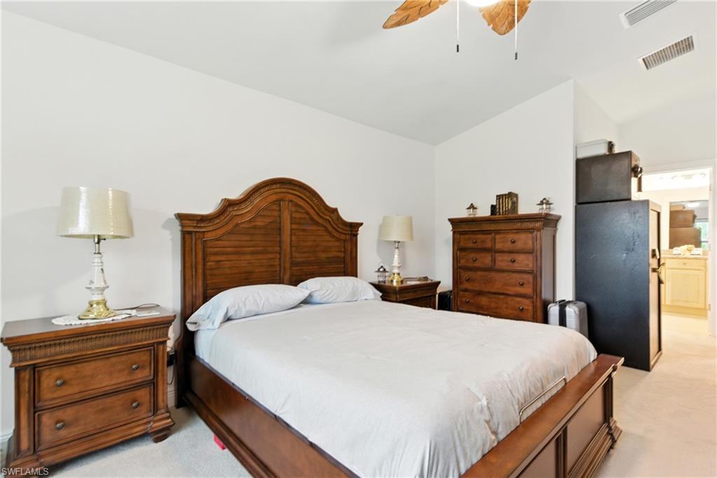 Bedroom featuring light colored carpet, ensuite bath, ceiling fan, and lofted ceiling