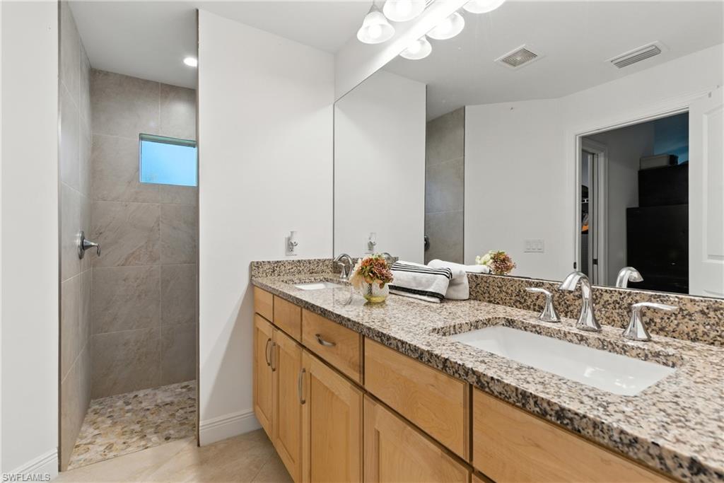 Bathroom featuring double vanity, a walk in shower, and light tile patterned flooring