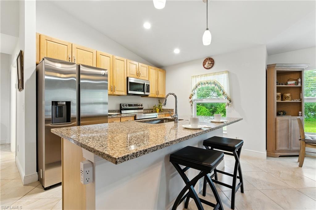 Kitchen featuring stainless steel appliances, light brown cabinets, light stone counters, lofted ceiling, and pendant lighting