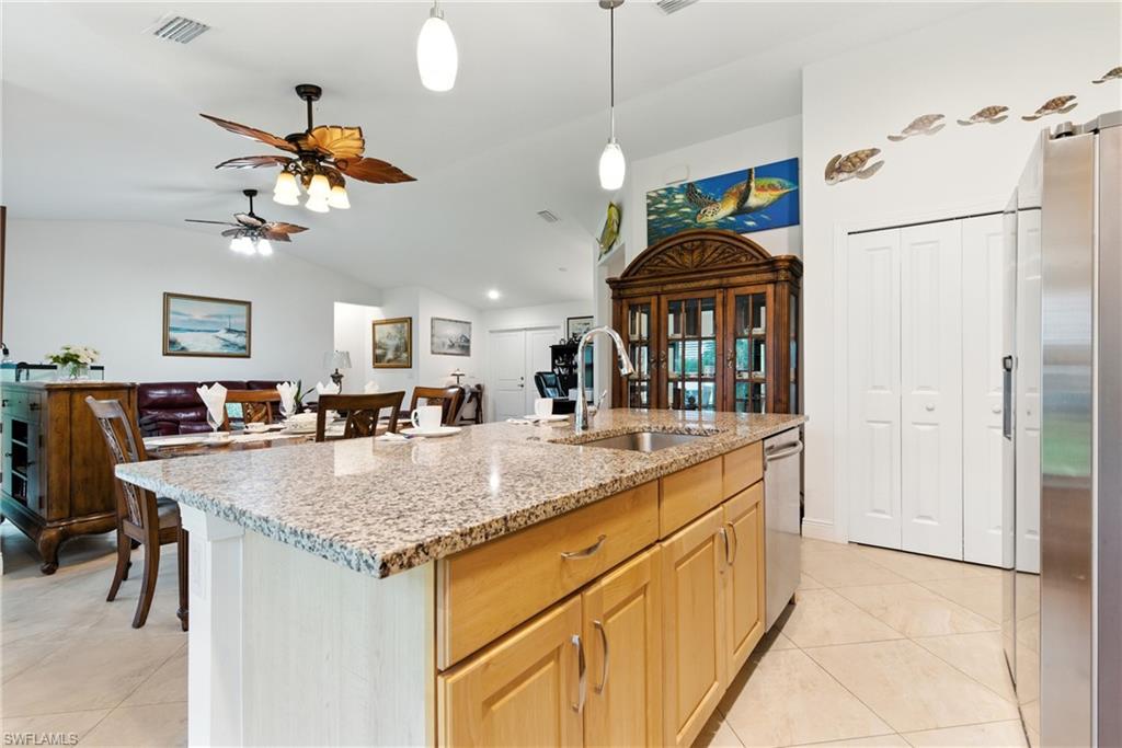Kitchen featuring lofted ceiling, light stone counters, appliances with stainless steel finishes, an island with sink, and a ceiling fan