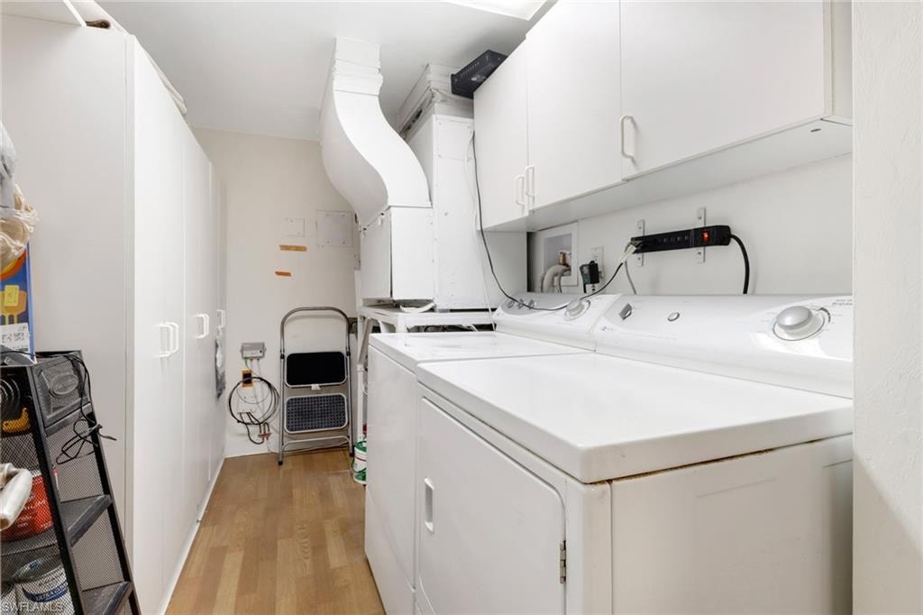 Clothes washing area with light wood-type flooring, washer and dryer, and cabinets
