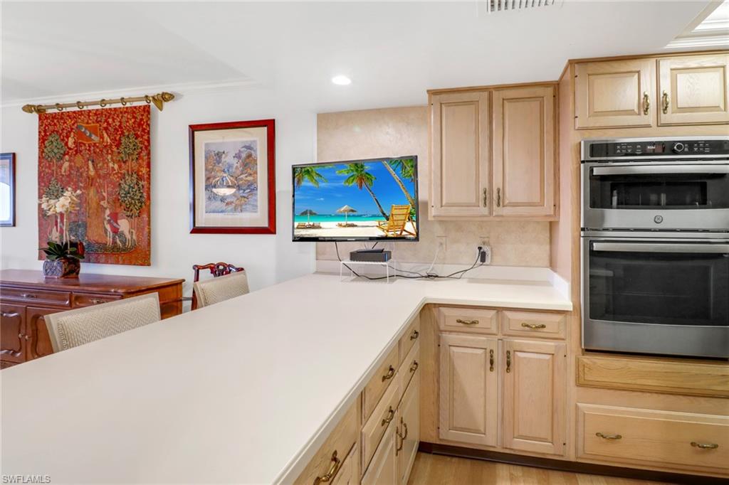 Kitchen with double oven, backsplash, light brown cabinetry, and light hardwood / wood-style flooring