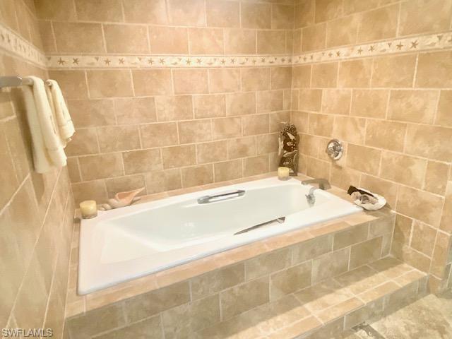 Bathroom featuring tiled tub, tile walls, and tile patterned floors